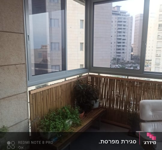 חלונות אלומיניום במרפסת סגורה עם נוף עירוני